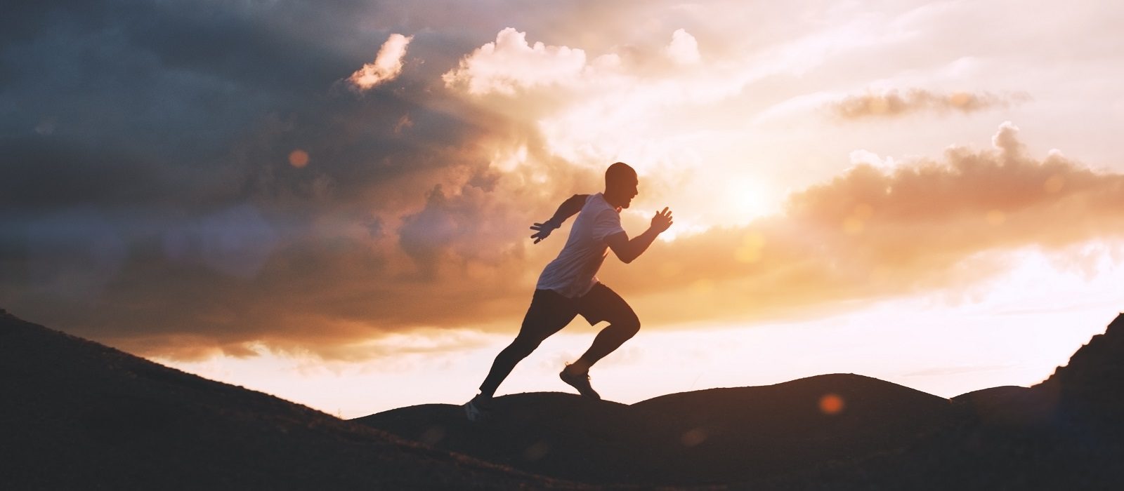 Athlete runs quickly through the hills outdoors at sunset